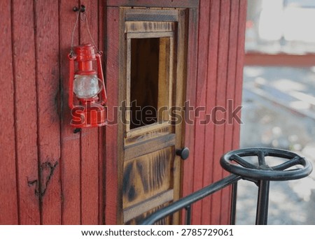 Red lantern hanging on a rustic model railway caboose with vintage wooden detail and shallow depth of field.