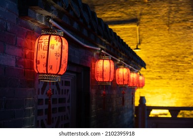 
Red Lanterns Hanging On The Wall Of The Chinese City At Night.Text Translation On Lantern: Blessing, Ancient Chinese Characters Of Various Blessings, Auspicious, Safety