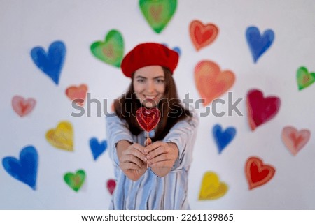 in red, a large lollipop in the shape of a heart in focus, a girl holding a candy against a background of colorful bright hearts, the concept of valentine's day, love
