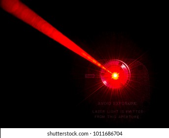 Red laser beam from a lab laser. Warning notice on front. Black background. Beam scatters near aperture.