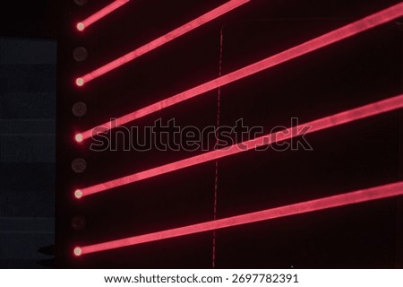 Red laser beams create a dynamic diagonal pattern against a dimly lit interior backdrop, predominantly red lighting Laser pattern suggests movement and perspective from the ground