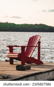 Red Lawn Chair Sitting On A Dock Infront Of A Lake 