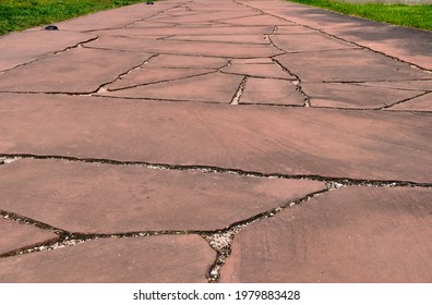 Red Layered Rough Surface Quartz Stone Sidewalk. Level Pavement. Gray Crashed Stone Joint Filler In Perspective View. Pattern And Texture. Parks And Outdoor. Walkway Paving. Green Grass At The Edges