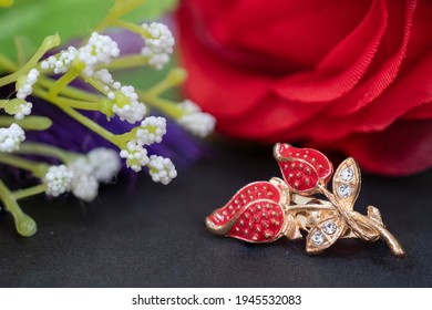 A Red Leaf Brooch In Fron Of A Red Flower
