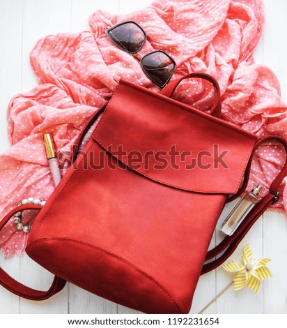 Red leather backpack with  accessories on a white wooden background