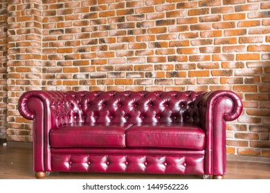 Red Leather Sofa Stands On The Brick Wall Background.