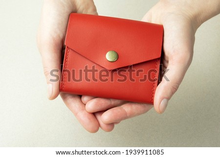 red leather wallet in open female hands close-up on gray background with shadows