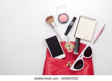 Red Leather Woman Bag With Cosmetic, Perfume, Smart Watch, Smartphone, Notepad, Pen On White Background, Top View