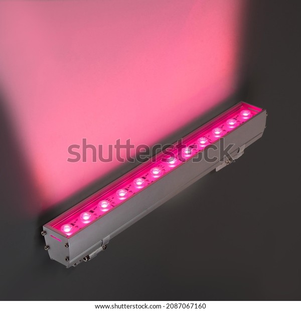 Red LED flood light in aluminum housing with\
wire on dark background.