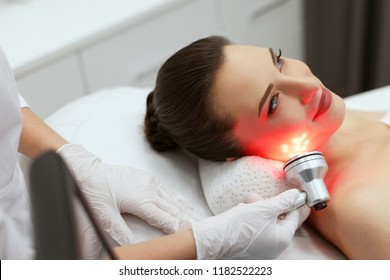 Red Led Light Treatment. Woman Doing Facial Skin Therapy 