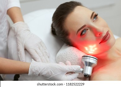 Red Led Light Treatment. Woman Doing Facial Skin Therapy 