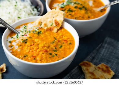 Red lentil soup with coconut milk and curry accompanied by basmati rice and naan bread on a dark blue background - Shutterstock ID 2251605627