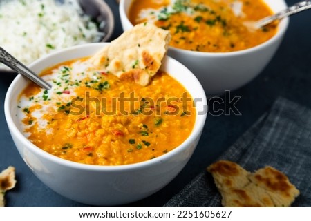 Red lentil soup with coconut milk and curry accompanied by basmati rice and naan bread on a dark blue background