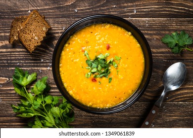 Red Lentil Soup Puree In Black Plate On Wooden Table. Top View.