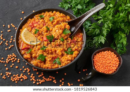 Red lentils dal in black bowl on dark slate table top. Lentils tomato dhal is indian cuisine dish with lemon and ciliantro. Indian food. Asian vegetarian meal