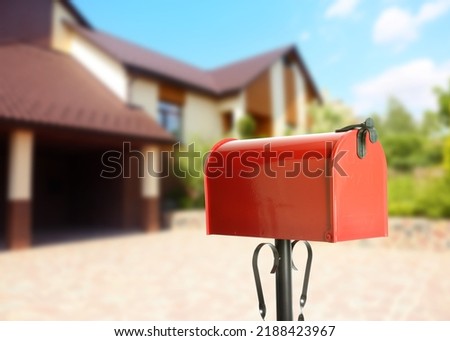 Red letter box and blurred view of modern house on sunny day