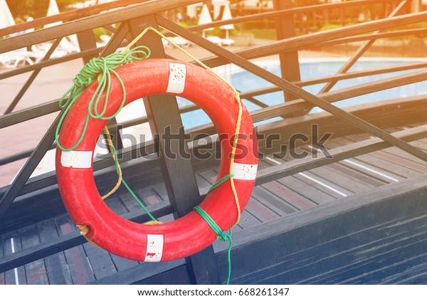 Red life buoy hangs on a wooden handrail near the\
pool, toned\
