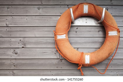 Red lifebuoy with rope on weathered wooden wall in port