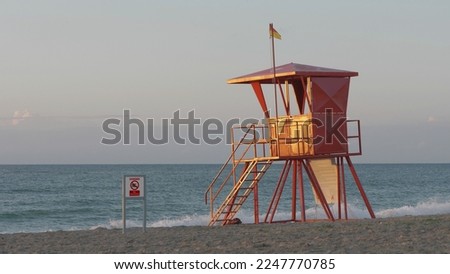 Red lifeguard tower and danger no swim warning placard on empty beach