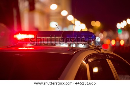 Red light flasher atop of a police car. City lights on the background. 