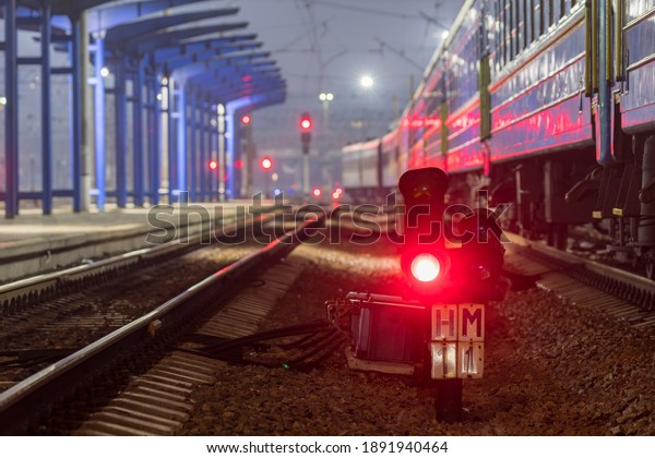 The red light of\
the traffic light signals a redirection signal for trains.  Train\
Station.  Night photo.