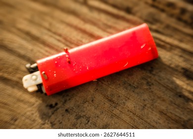Un encendedor rojo está tendido sobre una superficie de madera. El encendedor está sucio y tiene un residuo negro