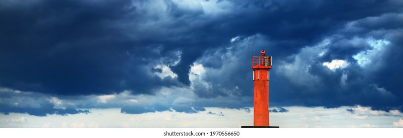 Red lighthouse with a solar battery. Dramatic blue sky, dark storm clouds. Baltic sea. Nature, weather, climate, alternative energy, power in nature, safety. Symbol of hope and peace