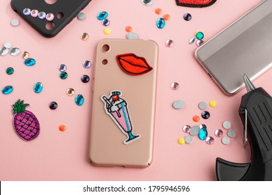 Red Lips And Cocktail Patches On Beige Phone Case. Heap Of Various Rhinestones And Glue Gun On Pink Background.