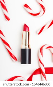 Red lipstick and candy canes top view composition. Beauty industry product concept. Makeup accessory and lollipops on white. Women pomade, cosmetology attribute. Christmas present idea.