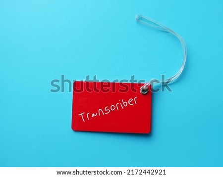 Red luggage tag on blue background  on with handwritten text TRANSCRIBER, means Transcriptionist or a person who listen to recorded audio video or other media and transcribe to writing words