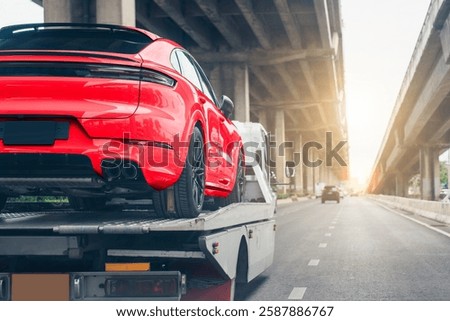 A red luxury sports car is loaded onto a tow truck, being transported on a highway under an overpass during sunset.  