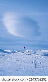 A red marking of a wintertrail in the snow and a lenticular cloud. Swedish Lapland.