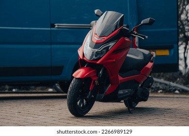 Red maxi scooter being delivered parked next to a blue delivery van, moped motorcycle two wheeled vehicle - Powered by Shutterstock