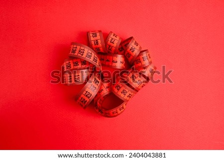 Red measuring tape on a red background. Tool for measuring length and volume. Tape for measuring in the clothing industry or the volume of the human body