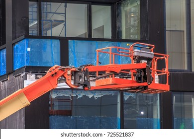 A red mechanical cherry picker is next to a building. A building is behind the lift.