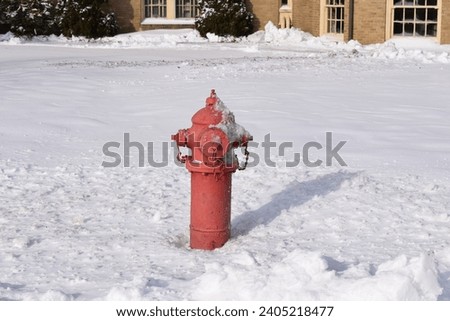 A red metal American fire hydrant in deep snow.  Outside a building, and casting a shadow onto the ground in the sunlight.  A very cold winter.  Pennsylvania, USA.  January 2019.