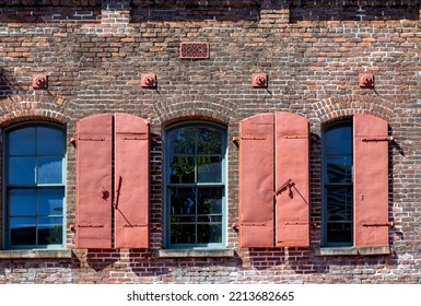 Red Metal Hurricane Shutters On A Vintage Brick Building With Arched Windows.