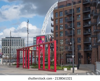 Red metal structure in front of residential building near London Designer Outlet, Wembley 12-March-2022. Background is Arch of Wembley Stadium.