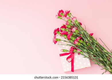 Red mini carnation and gift box. Concept of giving present at mother's day as surprise, flat lay, top view On pink Background.