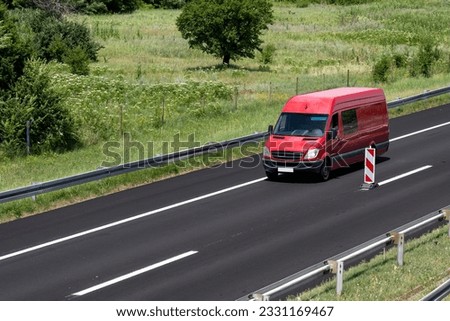 A red minivan is moving down the highway. Red delivery van on the highway. A red modern small package delivery van speeding down the highway to the suburbs of the city.