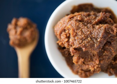 Red Miso Paste On White Bowl Viewed From Above With Spoon On Table Out Of Focus.