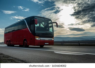 Red Modern Comfortable Tourist Bus Driving Through Highway At Bright Sunny Sunset. Travel And Coach Tourism Concept. Trip And Journey By Vehicle
