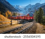 Red modern electric train traveling along a railway, winding through a stunning high mountains with snow-capped peaks and vibrant autumn trees in switzerland. Bernina Express in fall. Railway tourism