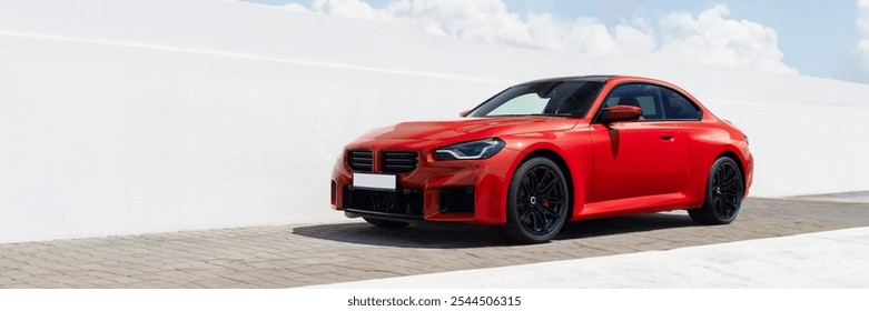 Red modern sports car standing against a white wall and sky. Minimalist white background.
