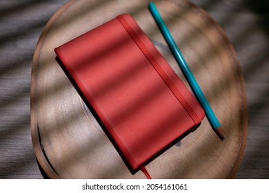 red moleskine with pencil on wooden background for mockup. flat notebook with elastic on shade of blind curtain