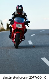 Red Motorcycle With Driver In Leather Suit While Driving On A Road With A Slight Side Position, Photographed From The Front.
