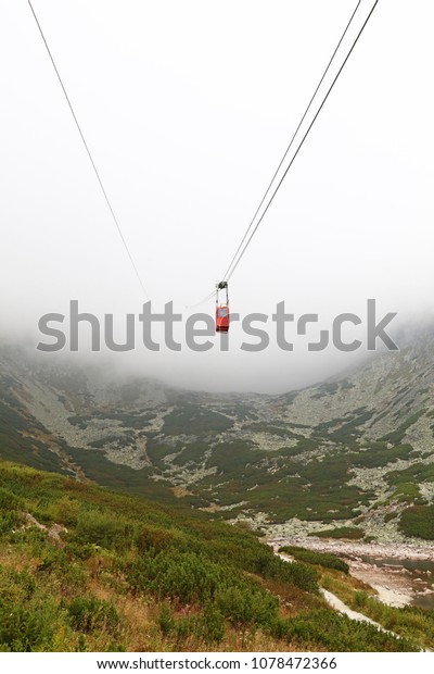 Red mountain cableway car lift in clouds and fog,\
low angle view