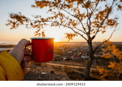 red mug in hand at dawn with a yellow tree - Powered by Shutterstock