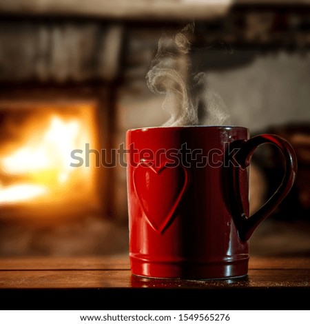 Red mug with hear on wooden board and free space for your text or decoration. Home interior with fireplace and warm light. Chrsitmas time and cold winter day. Copy space, Table background, Hot coffee 