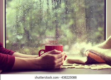 red mug of hot drink, when behind a window is rain / cozy home atmosphere - Shutterstock ID 438225088